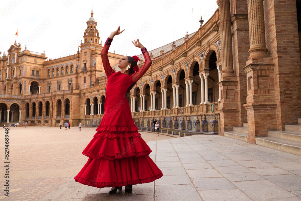 Beautiful teenage woman dancing flamenco in a square in Seville, Spain. She wears a red dress with ruffles and dances flamenco with a lot of art. Flamenco cultural heritage of humanity.