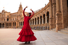 Beautiful Teenage Woman Dancing Flamenco In A Square In Seville, Spain. She Wears A Red Dress With Ruffles And Dances Flamenco With A Lot Of Art. Flamenco Cultural Heritage Of Humanity.