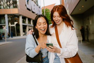 Young beautiful smiling redhead girl hugging cute happy asian girl