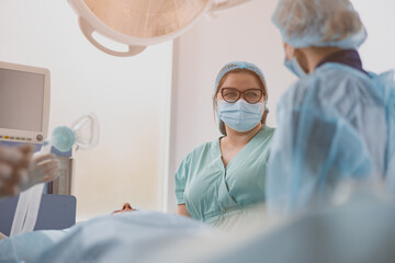 Wall Mural - Nurse assisting doctors during surgery in operation room of modern clinic. Blurred background