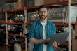 © Friends Stock - Male worker standing with laptop on warehouse with coffee machines