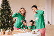 © Елизавета Старкова - An Asian family with two children in green pajamas cook together festive cookies celebrate the Christmas holiday in decorated house in winter. Mom dad son and daughter spend time together on vacation