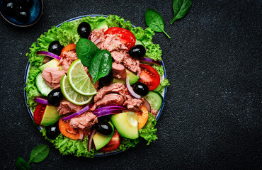 Tuna fish salad with avocado, tomato, cucumber, black olives, spinach, red onion and lettuce. Black stone kitchen table background, top view