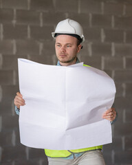 Wall Mural - engineer in a white helmet and a protective vest with a project in his hands is thoughtful and professional. A successful European designer or builder at the facility makes measurements of the room