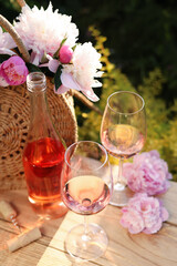 Poster - Bottle and glasses of rose wine near beautiful peonies on wooden table in garden