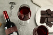 Glasses and bottle of red wine with chocolate on light marble table, above view