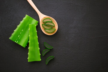 Wall Mural - Aloe vera leaf with slice in wooden spoon on black dark background , top view , flat lay.