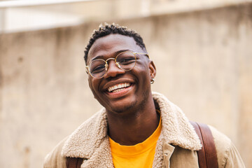 Close up portrait of african american teenage boy looking at camera smiling and laughing at univesity campus. Smart young student standing outdoors at college with backpack and googles. High quality