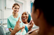 © Drazen - Close up of black woman looking her teeth in mirror after dental procedure at dentist's office.