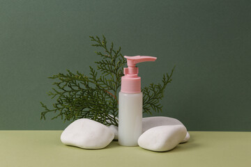 Aesthetic beauty still life. Bottle of cream or liquid soap  with stone and fir twig on two tone green background. Natural cosmetics, skin care