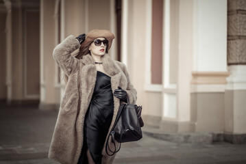 Wall Mural - Portrait of fashion woman in a warm fur coat, hat and sunglasses on a bright sunny day in the city