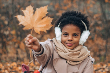 Portrait of a cute African-American girl with a maple leaf in her hands in an autumn park.Diversity,autumn concept.