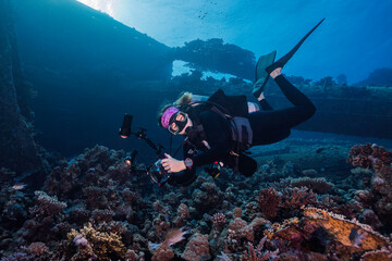 Wall Mural - An underwater photographer looking at the camera taking pictures on the reef with a ship wreck in the background