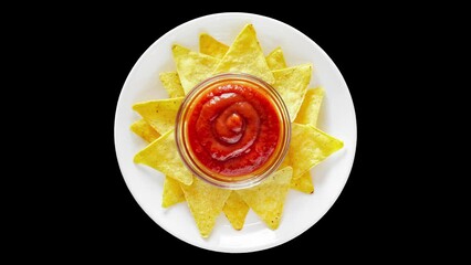 Wall Mural - Nachos whole with tomato salsa on white plate, top view, rotating isolated on black background, turning, close-up macro.
