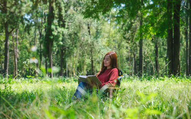Wall Mural - Portrait of a beautiful young asian woman reading a book while sitting on a camping chair in the park