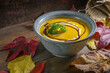 Autumn soup from red kuri squash with parsley garnish in a rustic bowl on a dark wooden table with colorful leaves for Thanksgiving or Halloween, copy space, selected focus