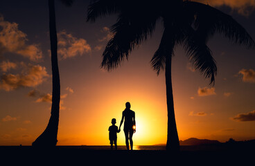 Wall Mural - Mother little child holding hands walking in a grass field at sunset.	
