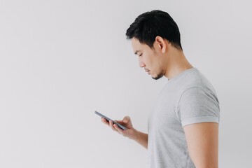 Wall Mural - Asian man seriously concentrated on smartphone isolated on white background.