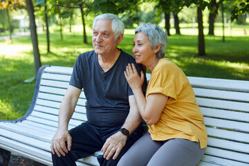 Older couple resting in park seated on bench enjoy talk