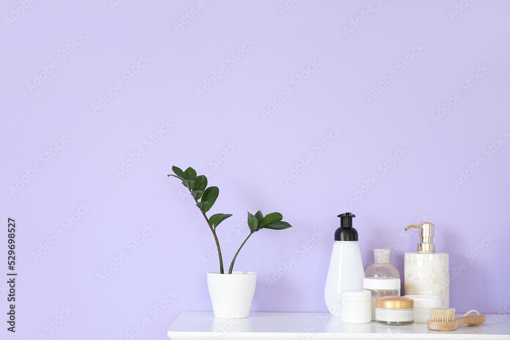 Houseplant and bath accessories on table near lilac wall