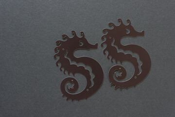 two grungy paper seahorses on dark gray board