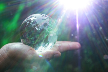 Human hand holding globe planet glass In green forest with bokeh nature lights. world environment day. concept for environment conservation, protect ecology earth and environmental eco-friendly life.