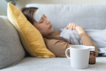 Wall Mural - Sick at home. Asian woman has fever sleep on sofa at home during quarantine virus.