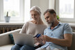 © fizkes - Happy middle aged elder family husband and wife shopping on Internet, paying for online purchase by credit card, using bank ecommerce app on laptop, resting on couch at home