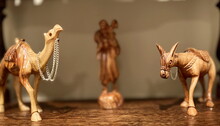 Wooden Figurines Of A Donkey And A Camel Stand On Both Sides Of The Photo. In The Center, In Full Blur, Is The Figure Of A Man On His Back With A Lamb. High Quality Photo