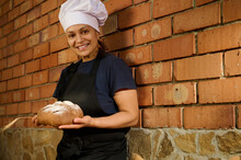 Beautiful Female Baker Posing With A Traditional Homemade Sourdough Wheaten Bread Against Red Brick Wall Background