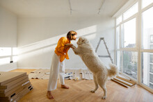 Young Woman Plays With Her Dog In Room While Making Repairing In Apartment. Fun During House Renovation And Friendship With Pets Concept