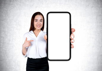 Poster - Businesswoman pointing at mockup big phone screen on grey concrete background