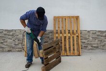 Image of a handyman at work who cuts pallets like pallets with an electric hacksaw. Do-it-yourself work and recycling of wooden boards.
