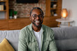 © Prostock-studio - Headshot of cheerful adult african american man in glasses and casual relaxing on sofa