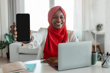 Poster - Happy black muslim woman with laptop showing smartphone with blank screen, recommending app, mockup