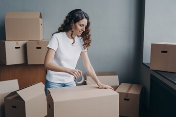 Wall Mural - Female sealing cardboard box parcel with adhesive tape on moving day. Removal service, relocation