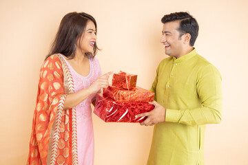 Happy young indian couple holding gift box celebrating diwali festival together isolated on studio background.