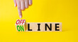 Offline and online symbol. Businessman hand points at turned wooden cubes with words Online and Offline. Beautiful yellow background. Business concept. Copy space.