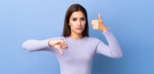 Wall Mural - Young caucasian woman over isolated background making good-bad sign. Undecided between yes or not