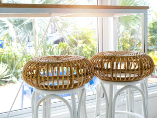 Two empty round rattan bar stool chairs near the table and glass window decoration in cafe with green tropical palm tree view outside.