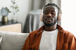 Calm african american man in wireless headphones sitting on sofa with closed eyes and listening to music, free space
