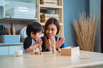 Mother is teaching her son to play with toys and clap for her son in the kitchen.