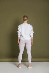 Wall Mural - Attractive blonde woman in white sweatshirt and leggings on green background. Mock-up.