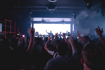 DJ performing in dark nightclub with crowd of people with their hands up