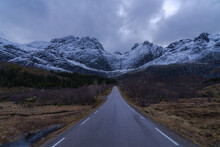 Empty Road Under Cloudy Sky And Snowy Mountains