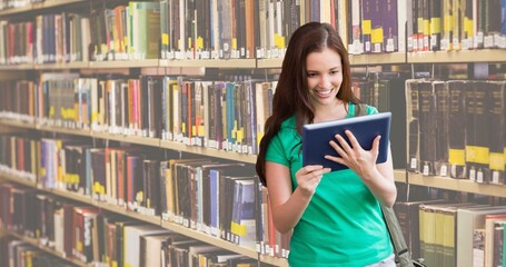 Poster - Smiling caucasian teenage girl reading book while standing against bookshelf in library