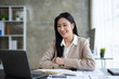 © amnaj - Beautiful Asian business woman using her laptop to work and enjoy working, taking note, reviewing assignment and smiling in the office.
