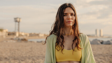 Wall Mural - Portrait of caucasian attractive cute woman looking to camera on the blur background. Staying in yellow top in morning at beach. Rest time concept 