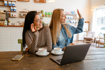 White women waving hands and using laptop while drinking tea in cafe