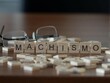 machismo word or concept represented by wooden letter tiles on a wooden table with glasses and a book